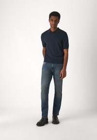 Polo à manches courtes bleu marine avec un ourlet côtelé, associé à un jean bleu délavé et des bottines noires. Design simple, couleurs unies.