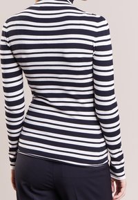 Maglietta a maniche lunghe a righe blu navy e bianche con collo a cono. Tessuto morbido ed elasticizzato con un design aderente. Presenta righe orizzontali in contrasto.