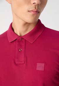 BOSS merk poloshirt in donkerroze met een klassieke kraag, een twee-knopen sluiting en een gestructureerde stof met een subtiele logo patch.