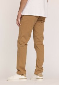 Chinos beige avec une coupe droite, en coton, et une texture lisse. Associés à des baskets blanches avec des accents beiges.