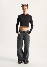 Black cropped long-sleeve top with script detail; gray checkered baggy pants; black shoes with cartoon accents; plain background.