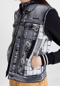 Jeansväst med en blekt svart och vit design, prydd med blommig broderi, strukturerade lappar, hög krage och tryckknappar.