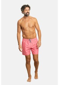 Pantalones de natación de tela rosa claro con cinturilla elástica y cordón gris. Modelo descalzo, con una postura natural y relajada.