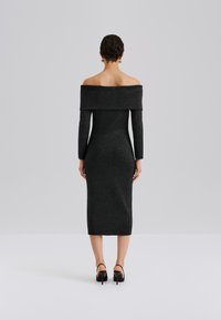 Zwart, off-the-shoulder jurk met lange mouwen, slim fit, knie-lengte, glinsterende textuur, gecombineerd met zwarte hoge hakken.