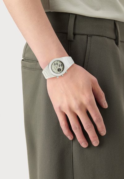 White wristwatch with a textured silicone strap, round case, and light gray face featuring three chronograph dials, worn on a hand.