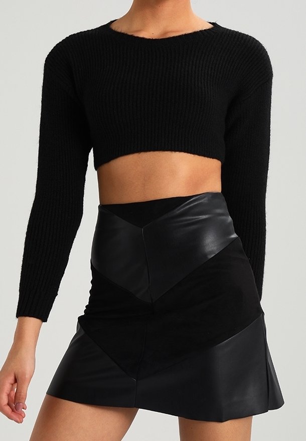 Schwarzer, verkürzter Pullover mit geripptem Muster und langen Ärmeln, kombiniert mit einem schwarzen Minirock aus Leder und Wildleder mit einem Zickzackdesign.