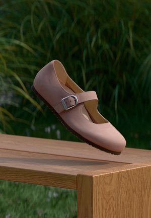 Hele-roosa Mary Jane kinga hõbedase pandlaga, mis hõljub puidust pingi kohal, taustal roheline hägune muru.