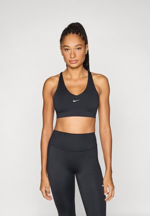 Zwarte sportbeha met een V-hals ontwerp en brede bandjes, met een klein wit Nike-logo gecentreerd op de borst. Gladde stoftextuur.