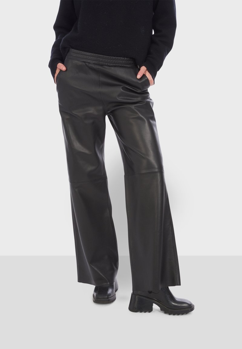 Pantalon large en cuir noir à la texture lisse, taille haute et poches latérales. Associé à des bottines noires, dotées d'une semelle épaisse.