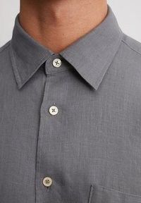Camicia di lino grigia con colletto a polo, dotata di due bottoni sulla parte anteriore e di una tasca a toppa sul petto.