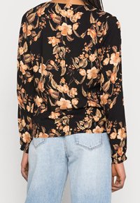 Blusa a maniche lunghe con uno sfondo nero e fantasie floreali in beige e pesca chiaro, con polsini arricciati e una vestibilità comoda, abbinata a jeans chiari.