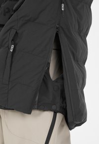 Svart isolerad jacka med dragkedja fram, tryckknapps-stängning och elastisk nederkant. Har sidofickor och ett strukturerat yttertyg.