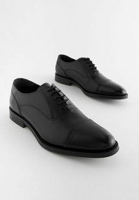 Schwarze Lederschuhe mit glatter Oberfläche, runder Zehenform und fünf Ösen. Verfügt über ein dezentes, geschwungenes Design an den Seiten und einen niedrigen Absatz.