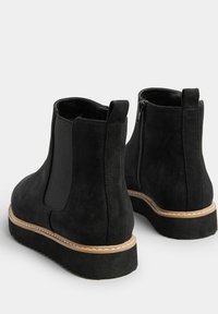 Czarne botki za kostkę o gładkiej zamszowej fakturze, z bocznymi elastycznymi panelami, zamkiem błyskawicznym i kontrastującą beżową krawędzią podeszwy. Okrągły czubek.