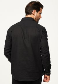 Schwarzes Langarmshirt mit Button-Down-Kragen, aus Baumwollstoff, taillierte Passform und zwei Knopfakzente an jedem Ärmelbund.