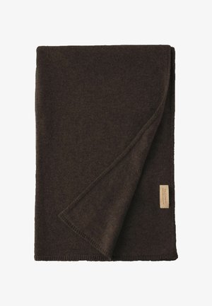 Coperta piegata in lana marrone scuro con angolo sollevato che mostra la trama morbida e un'etichetta rettangolare sul bordo.