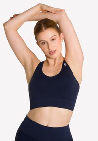 Granatowy stanik sportowy o dopasowanym kroju, szerokich ramiączkach i gładkiej fakturze. Zawiera logo na ramieniu i krótką długość.