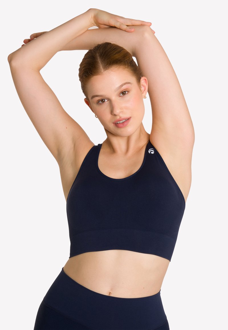 Granatowy stanik sportowy o dopasowanym kroju, szerokich ramiączkach i gładkiej fakturze. Zawiera logo na ramieniu i krótką długość.