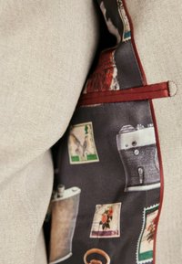 Svijetlosivi tkanina riblja kost s tamno uzorkovanom podstavom koja sadrži vintage kamere, markice i flaše. Akcentirana tamnocrvenim obrubom.