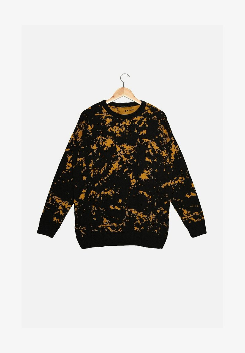 Pull en tricot noir avec un motif éclaboussé irrégulier jaune moutarde, manches longues, col rond, suspendu à un cintre en bois sur fond blanc.