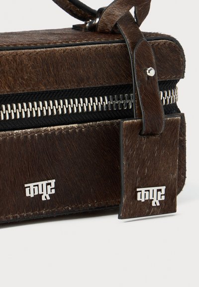 Brown leather bag with a textured, fur-like finish, silver zipper, and a rectangular tag displaying a logo. Features a black fabric accent.