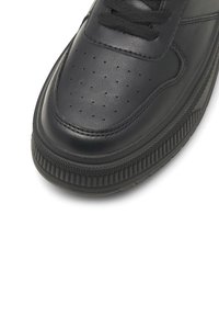 Sneaker din piele neagră, cu vârf perforat, șireturi plate și talpă din cauciuc texturată cu striații orizontale. Design curat și minimalist.