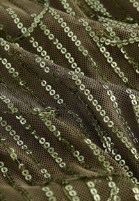 Tessuto a rete verde oliva con pratiche decorate da paillettes disposte in linee ondulate, con una superficie texturizzata e un leggero riflesso luminoso dato dalle paillettes.