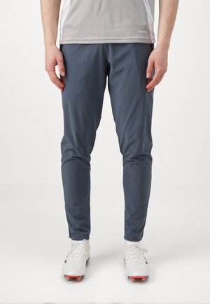 Graue Sporthosen mit slim fit, aus leichtem Material, kombiniert mit weißen Schuhen mit roten Akzenten.