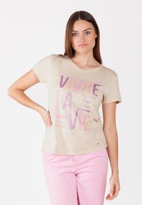 T-shirt beige à manches courtes,col rond, avec un texte en paillettes roses et violettes. Tissu doux au tomber décontracté.