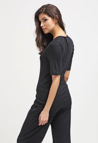 Top nero aderente a maniche corte con una texture liscia e un collo rotondo, mostrato dal retro. Design minimalista.