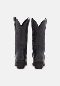 Un par de botas de vaquero de cuero negro con patrones decorativos bordados, lengüetas para tirar y tacones apilados, vistas desde atrás sobre un fondo blanco.