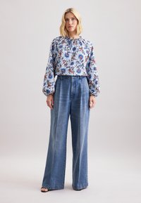 Blusa floreale con motivi blu, rossi e bianchi; scollatura arricciata. Pantaloni in denim blu a gamba larga, a vita alta, fit ampio, con pieghe.