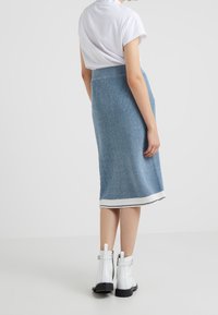 Stickad, blå midi kjol med ribbad textur, med en vit randad fåll. Matchas med vita ankelstövlar och en kortärmad vit topp.