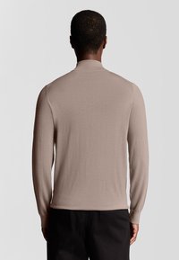 Beige, leichtes Langarmhemd mit einem schlichten Design und geripptem Kragen. Es zeigt eine glatte Textur und eine figurbetonte Silhouette.