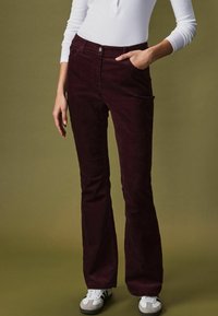 Bordeaux velour flared bukser med forlommer, 5-knap lukning, parret med hvid langærmet top og grå sneakers. Tekstureret stof.