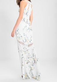 Abito lungo floreale bianco con corpetto aderente, stampa floreale in morbido giallo e verde, dettagli in pizzo vicino all'orlo e design senza maniche.