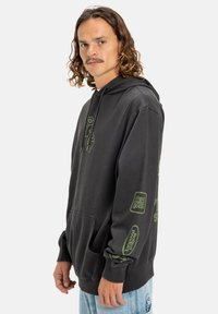 Zwarte hoodie van zachte stof, met een kangoeroezak, groene grafische prints op de voorkant en mouwen, en geribde manchetten.