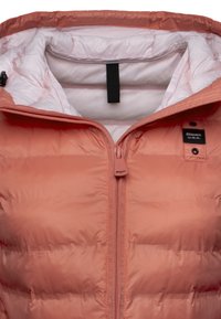 Lichte perzikkleurige pufferjack met rits, voorzien van een zachte binnenvoering en een label op de schouder, ontworpen voor warmte.