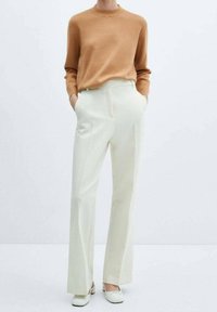 Suéter de punto beige con escote redondo, combinado con pantalones blancos de talle alto y corte entallado, con bolsillos laterales y diseño de pierna recta.