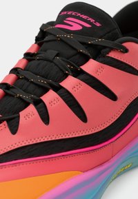 Baskets Skechers noires et roses avec semelle multicolore, lacets noirs avec couture orange et logo rose sur la languette.