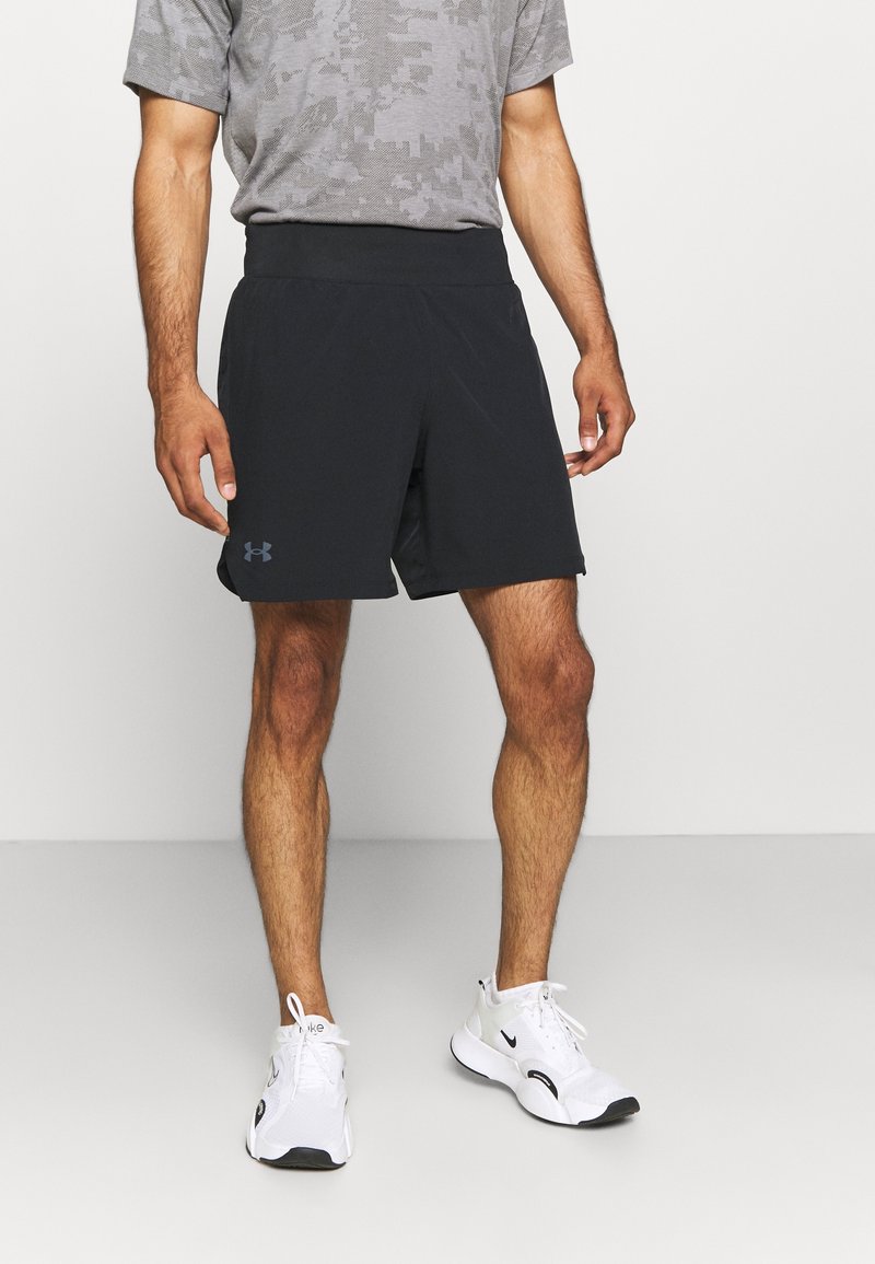 Shorts atléticos negros con una banda elástica suave en la cintura, hechos de una tela ligera, combinados con una camiseta gris estampada y zapatillas blancas.