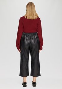 Bordeaux gebreid pullover met lange mouwen, gedragen met zwarte leren cropped broeken met een elastische tailleband en een gladde textuur.