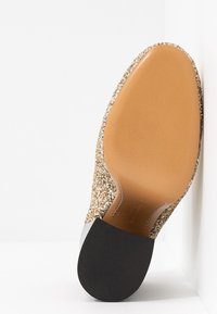 Semelle dorée scintillante avec un fond lisse couleur chêne ; comporte un talon en caoutchouc noir et un design élégant argenté au niveau du bout.