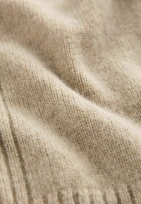 Beige neulekangas, jossa on pehmeä, tekstuuri pinta, hienovarainen nauha kuvio ja ohuet kuidut yhteensuuntautuina lämpimyyden takaamiseksi.