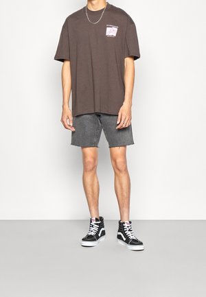 Brown oversized t-shirt with pocket graphic, gray denim shorts with frayed hem, and black high-top sneakers. Simple design and casual fit.