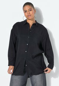 Camicia nera oversize realizzata in tessuto leggero, con colletto a punta, bottoni frontali e una superficie leggermente testurizzata.