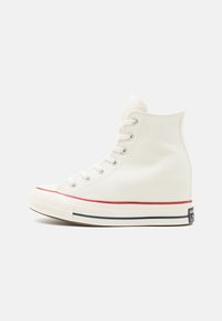 Hvit høyhælte kanvassneaker med sølvfargede snorer, rød og marineblå stripet såle og gummikappe. Glatt tekstur, klassisk snøredesign.