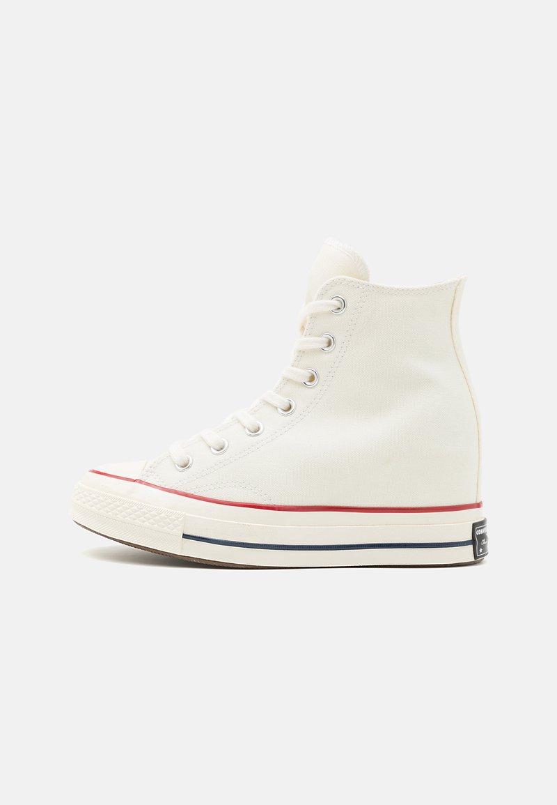 Hvit høyhælte kanvassneaker med sølvfargede snorer, rød og marineblå stripet såle og gummikappe. Glatt tekstur, klassisk snøredesign.