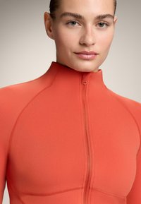 Rode atletische zip-up top met een hoge kraag, naadloos ontwerp en strakke pasvorm. Heeft zichtbare stiksels en een voorste ritssluiting.