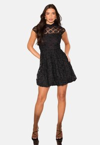 Černé krajkové šaty s dobře padnoucími korzetem, květinovým vzorem, vysokým výstřihem a rozšířenou sukní; mají krátké rukávy a boční kapsy.